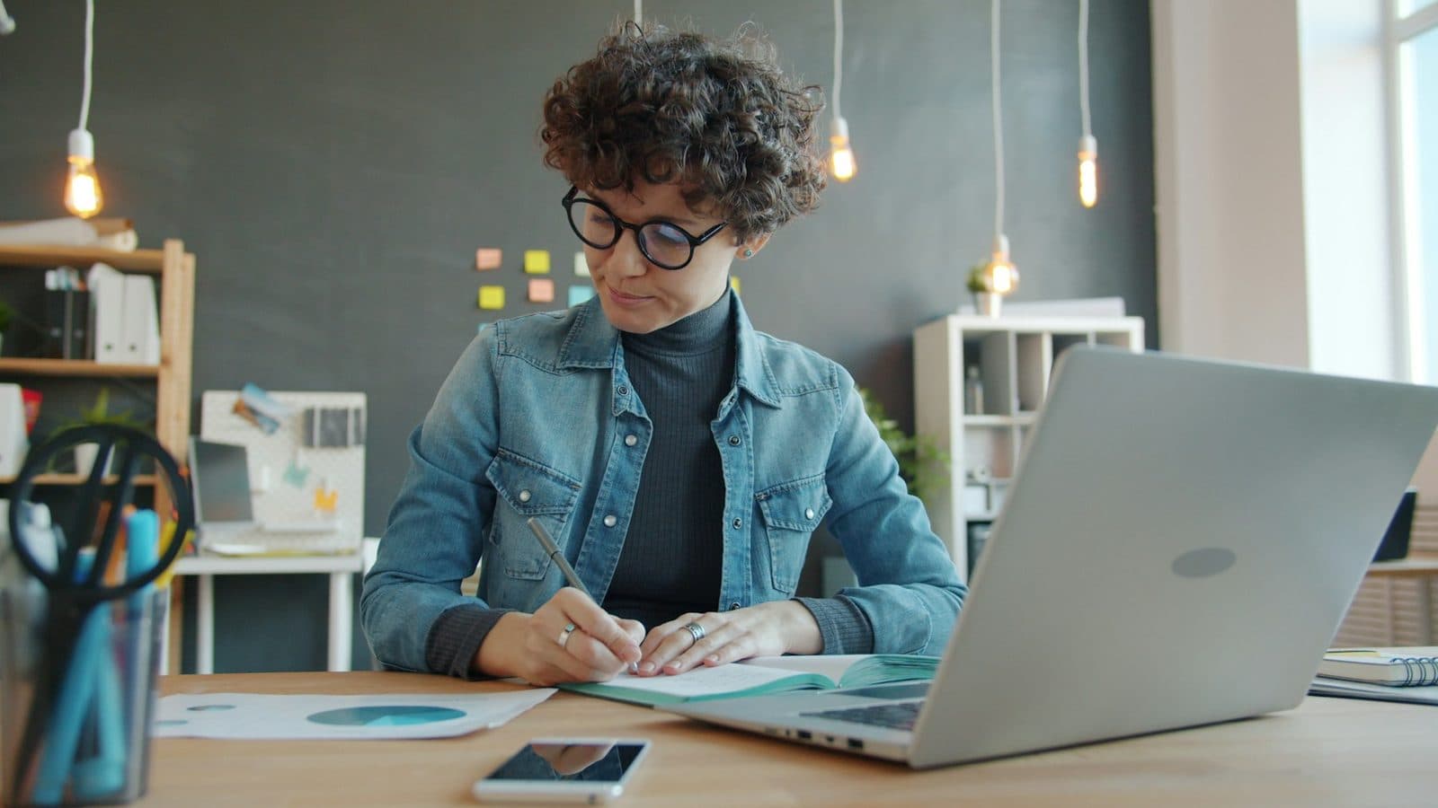 A salesperson writing follow-up notes at her desk next to a laptop and phone