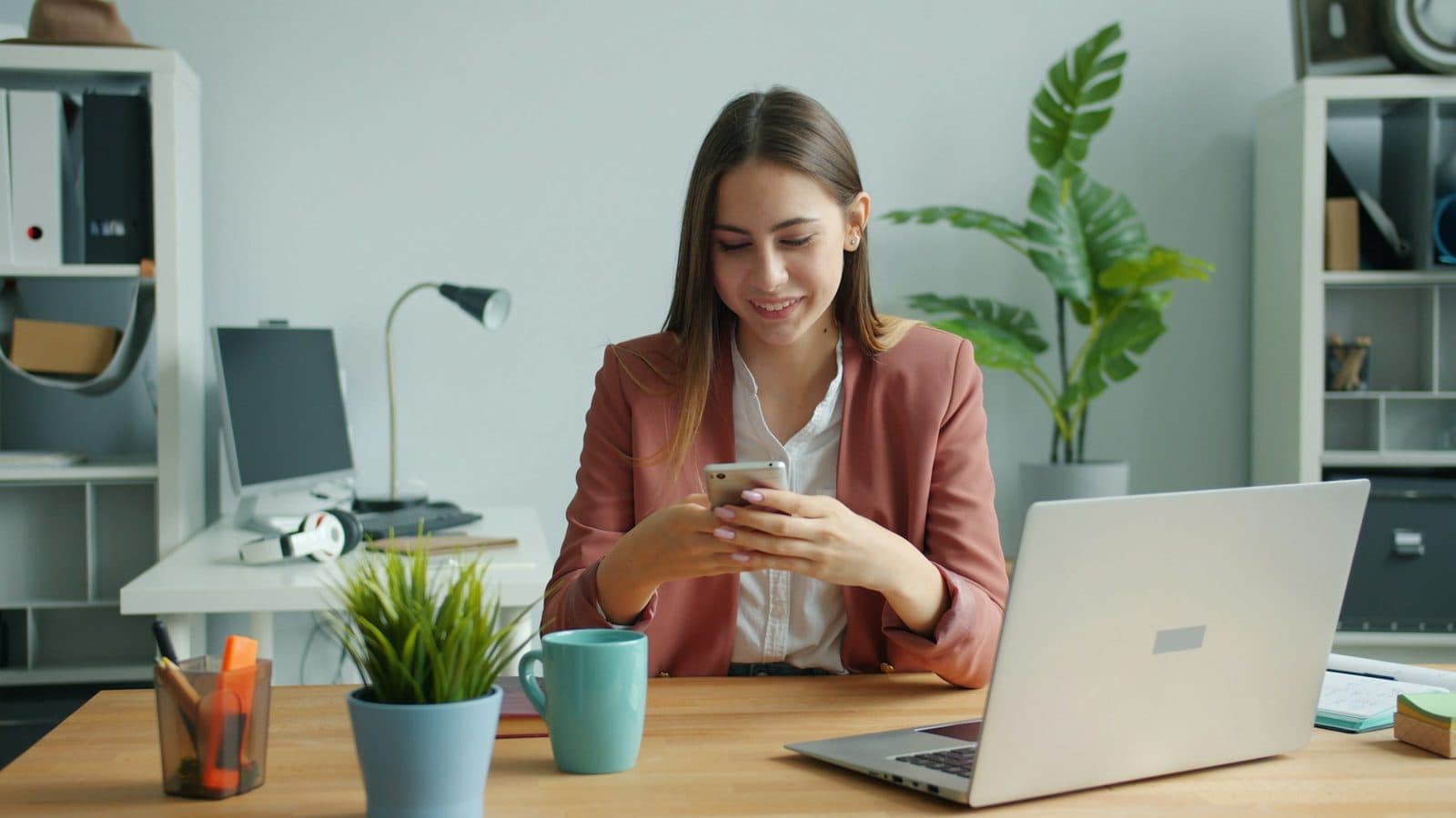 A professional smiling at her phone while answering a customer message at her desk